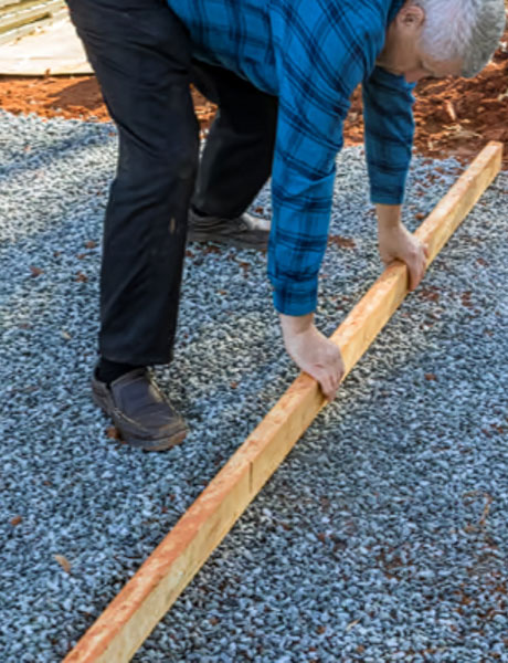 A photo of a man leveling a gravel pad - part of site prep and shed site inspection services
